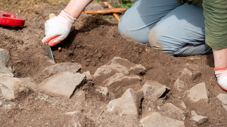Person with gloved hand digging through ruins