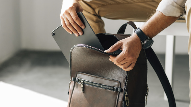 A person pulling a slim black device from a brown leather bag