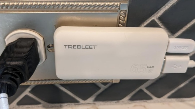 A white Trebleet Ultra Thin 65W USB-C Charger is attached to a wall outlet that has some very fancy trim