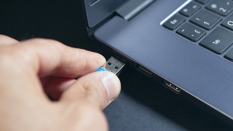 Close-up of a person plugging a USB flash drive into a laptop