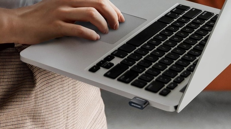 Close-up of a person working on a laptop with a Samsung Fit Plus USB drive connected to it