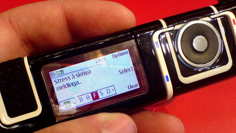 Person holding Nokia 7280 cellphone in front of red background
