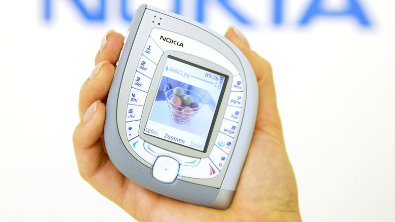 Person holding Nokia 7600 at technology trade fair with blurry Nokia logo in background