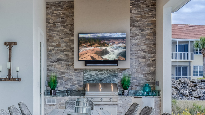 A TV mounted on a plaster wall in an outdoor space above a barbecue