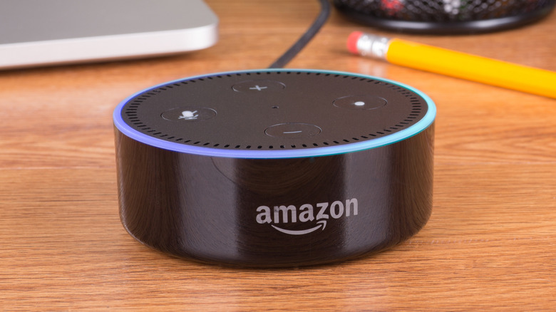 An Amazon Echo Dot sitting on a desk, a penci and the edge of a silver laptop can be seen behind it