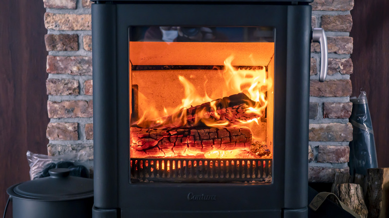 A black heater with several burning logs sits in front of a stone foundation in what appears to be the inside of a home