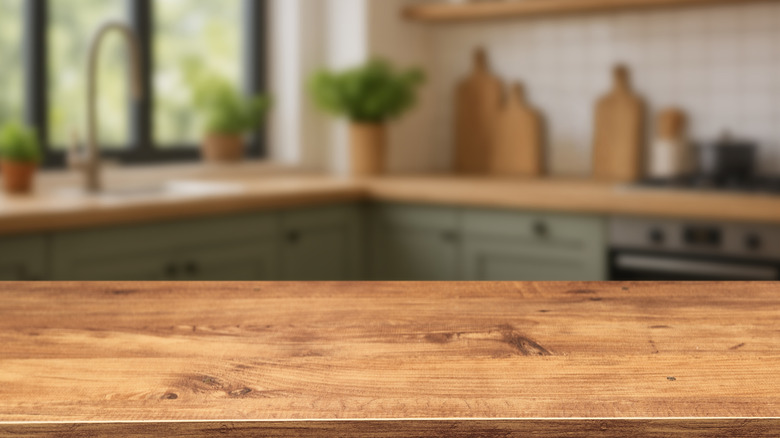 Wooden table top in a kitchen with cabinets, plants, and a window