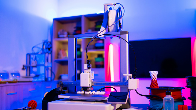 3D printer and filament kept on a table inside a room with cabinets and a TV in the background