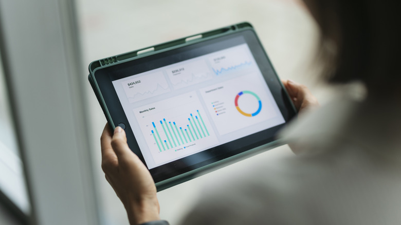 Person holding tablet displaying analytics dashboard with charts and graphs
