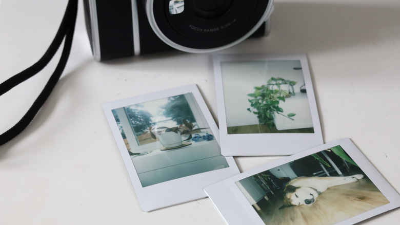 A camera sitting next to three instant photographs.