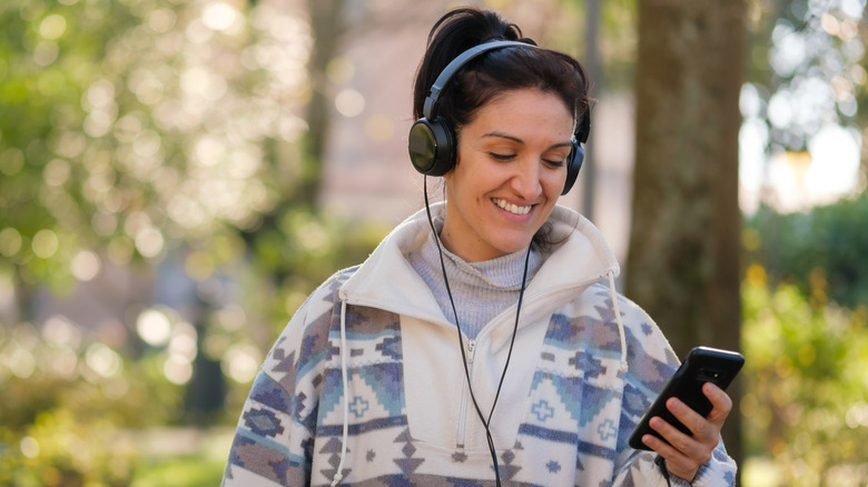 A woman smiling as she wears a pair of wired headphones connected to her phone.
