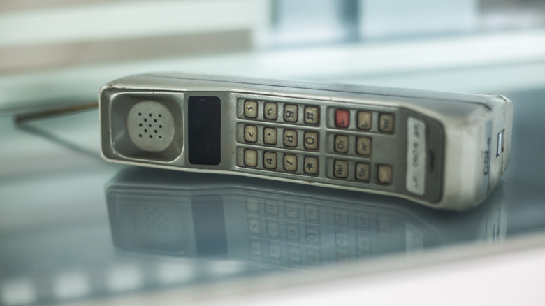 An old Dynatac mobile phone laying on its side on a glass table.