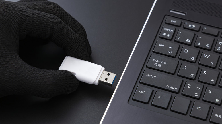 A gloved hand inserts a USB flash drive into a laptop.