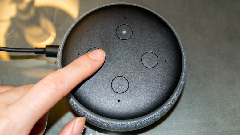 Finger pressing a button on top of an Amazon Echo Dot smart speaker.
