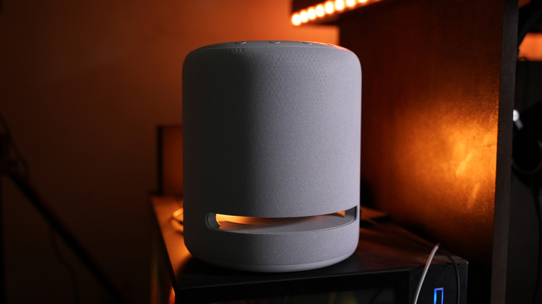 Amazon Echo Studio smart speaker sitting on a shelf under warm desk lighting.