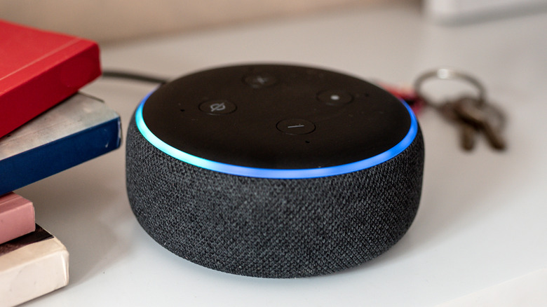 Amazon Echo Dot smart speaker with a blue light ring sitting beside books and keys.