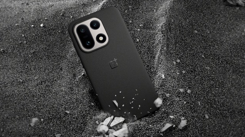 Black OnePlus 15 falling into black sand and rocks showing rear