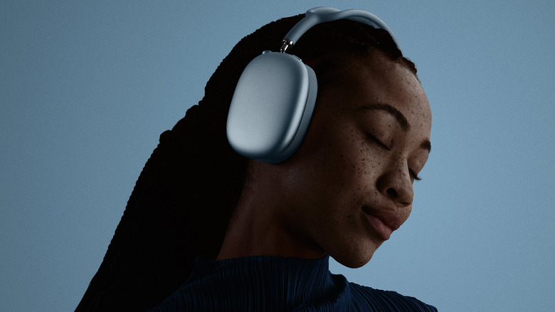 A young woman wearing with the Apple AirPads Max 2 headphones with her eyes closed on a blue background.