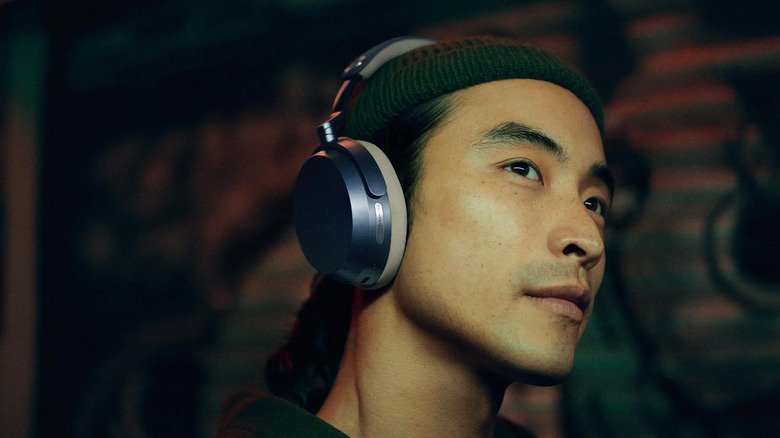 A young man wearing a beanie and the Sennheiser Momentum 5 Wireless headphones with graffiti in the background.