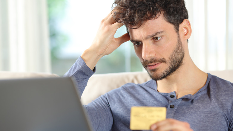 a person holding a credit card in hand while looking at a laptop