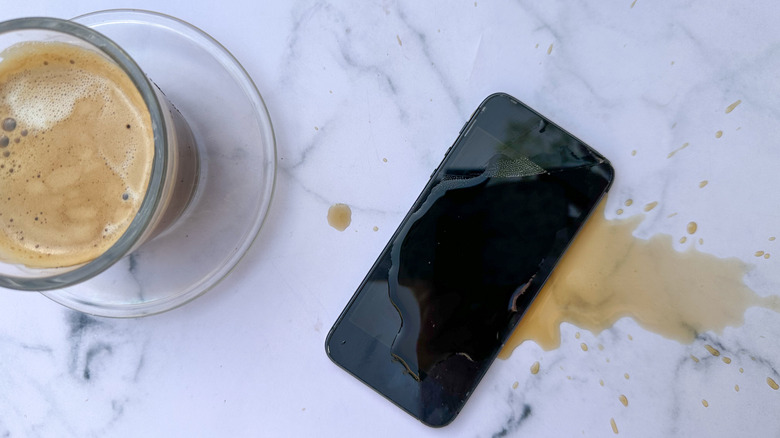 A phone on a countertop with coffee spilled on it.