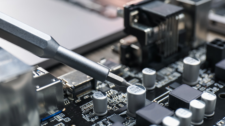 Person using screwdriver to repair part on motherboard.