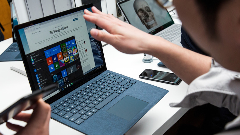 Person using touchscreen on blue Microsoft Surface Laptop.