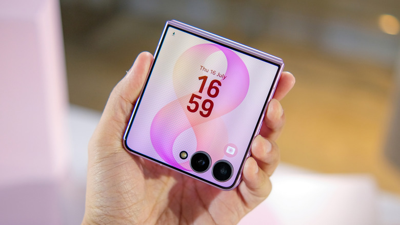 A purple Galaxy Z Flip is held in a user's hand, the device displays the time