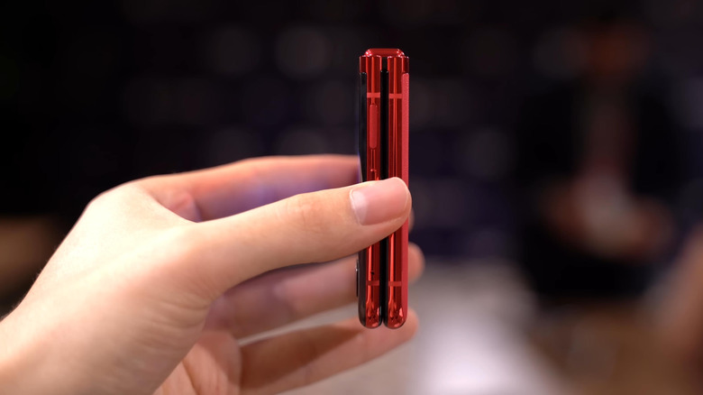 A red Motorola Razr smartphone is fully closed as it's held in a user's right hand