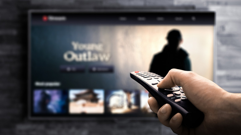 A person holding a remote with a blurred TV showing a figure obscured in darkness