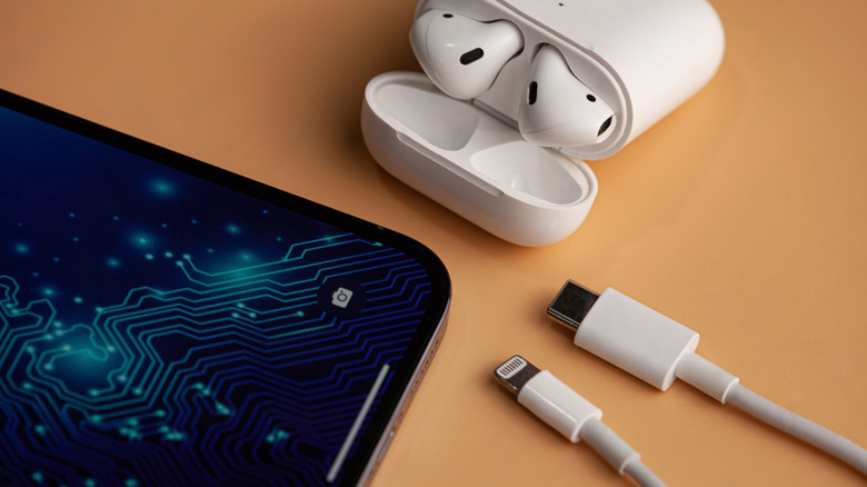 iPhone, airpods, and two charging cables kept on a wooden table