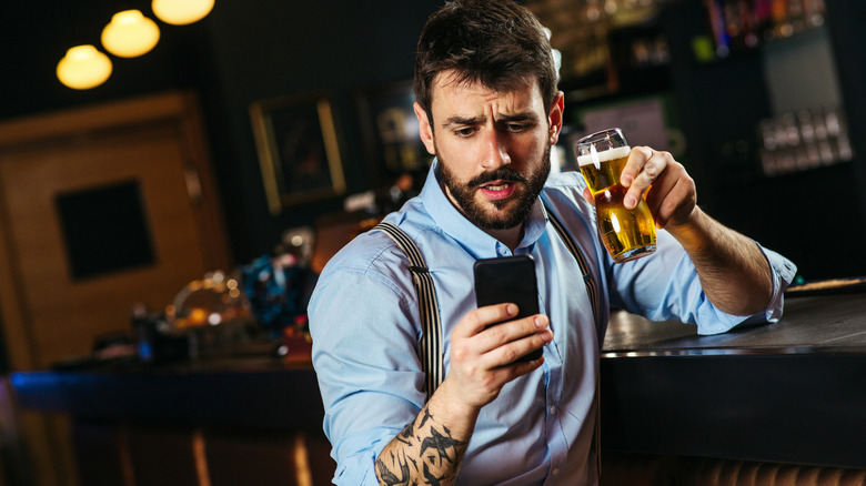 An individual holding a beer in their left hand and a smartphone in their right hand