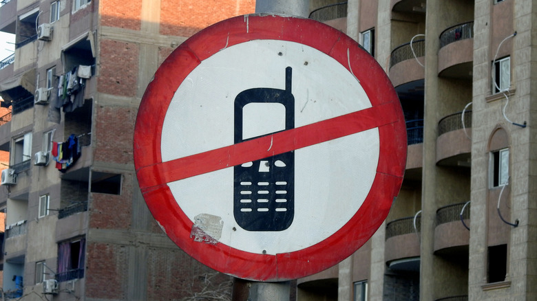 A sign in a public place showing a drawing of a cellphone with a red slash through it, suggesting that cellphones likely cannot be used in the area