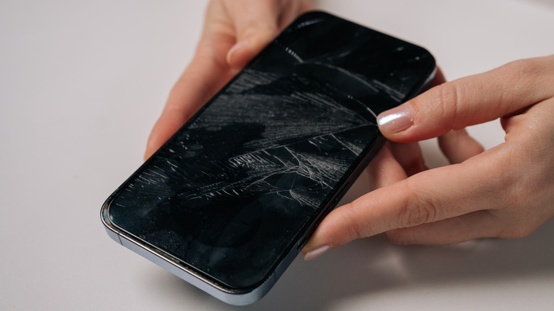 A woman holding a phone with a cracked screen