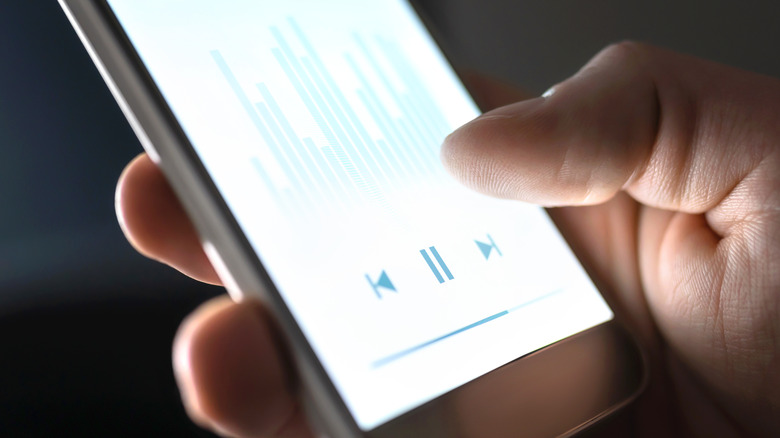 A hand holding a smartphone displaying a media player with a spectrum analyzer.