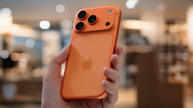 A close up shot of a hand holding an orange iPhone 17 Pro Max with a blurred background.