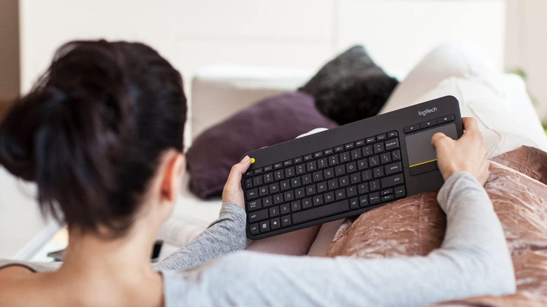 A woman using the Logitech K400 keyboard while laying on a couch
