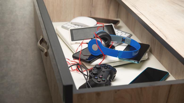 A drawer full of dusty old tech such as headphones, smartphones, and control devices