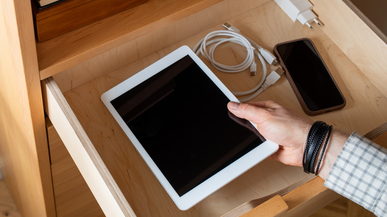 A person pulling a tablet out of a drawer where it is stored among other tech