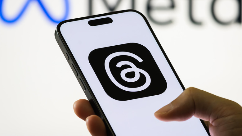 Hand holding a phone with Threads app logo shown