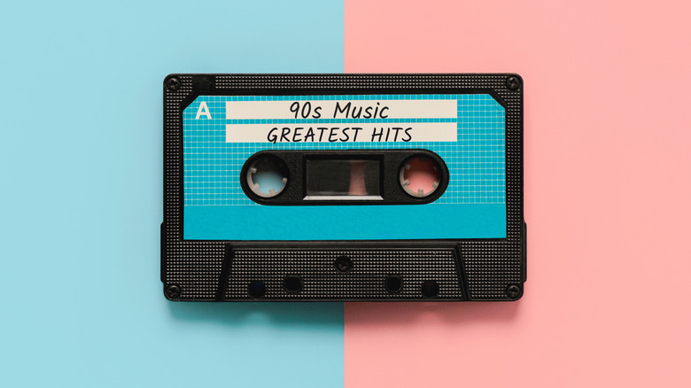 A black cassette labeled "90's music greatest hits" sits against a pastel blue and pink backdrop