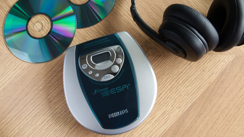 A small portable Philips CD player sits on a wooden surface next to a pair of black headphones and two CDs
