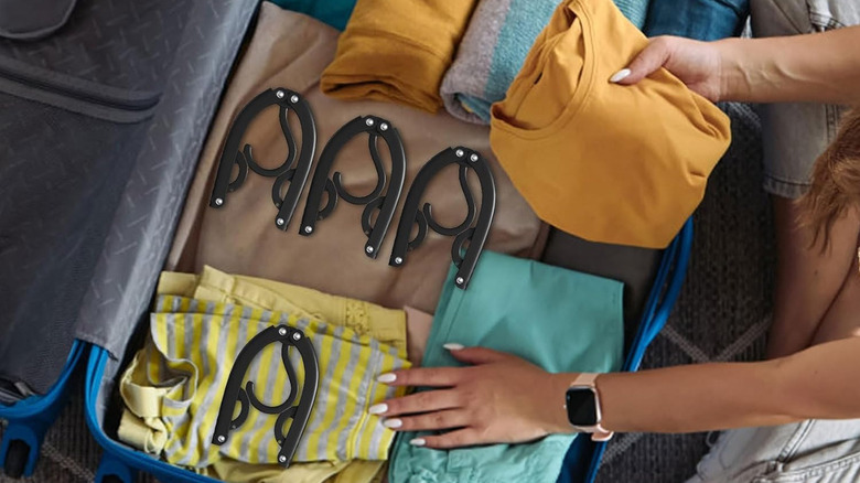 A person filling a suitcase with clothes and foldable hangers.