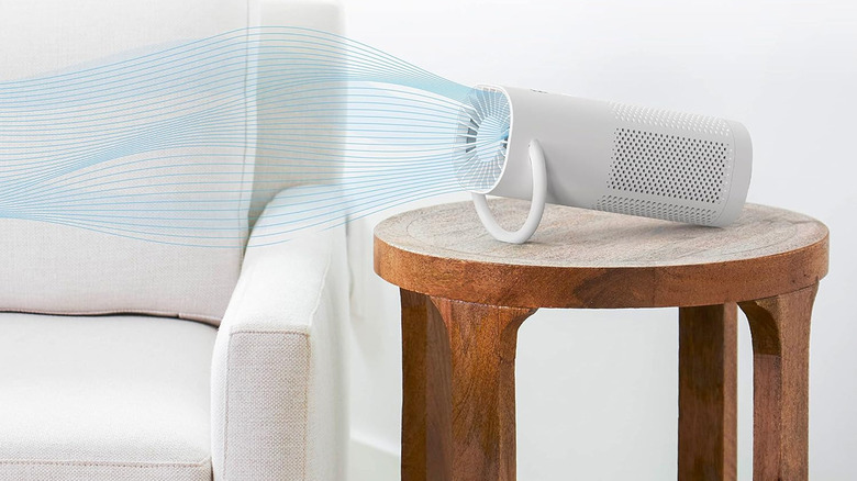 A portable air purifier on its side on a table by a chair.