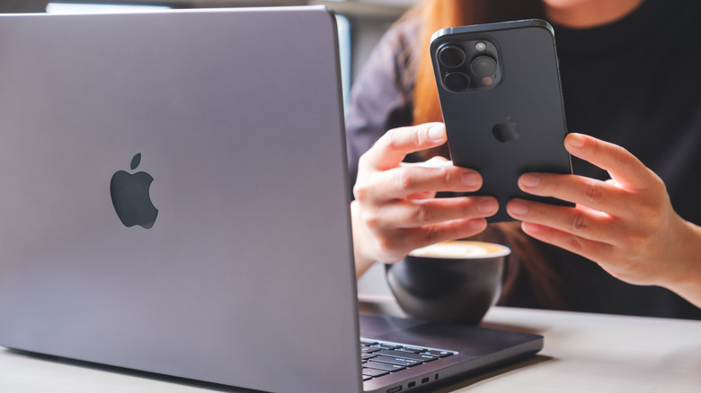 A woman using Iphone 15 Pro max smartphone and MacBook laptop computer