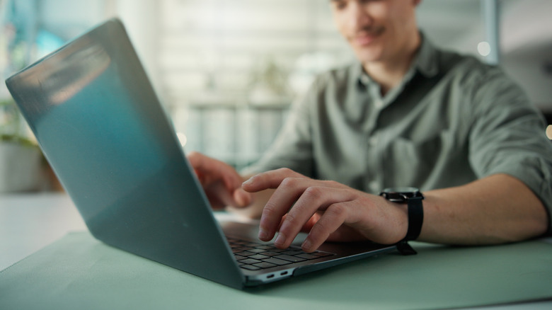 Person sitting at desk typing on laptop computer.