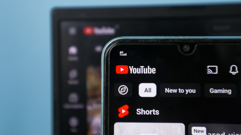 A close up shot of YouTube on a phone in the foreground and on a desktop in the background