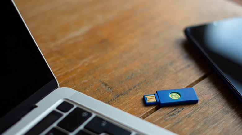 A security key on a table in between a laptop and smartphone
