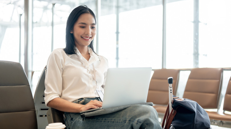 A woman using a laptop while sitting in an airport terminal.