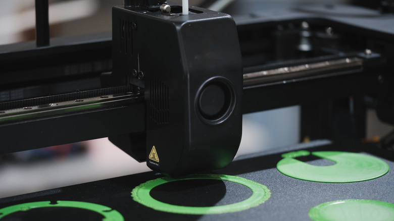 3D printer printing the first layer of a new project with a lime green filament.